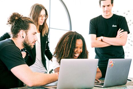 Zwei Frauen und zwei Männer schauen an einem Tisch auf zwei Laptops